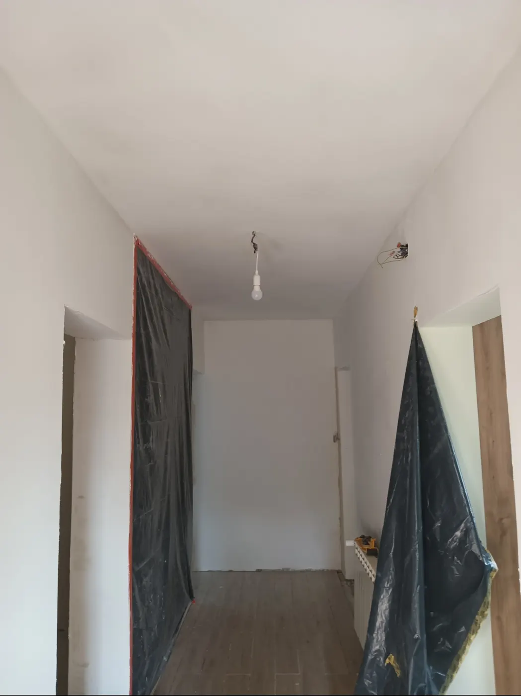 Korytarz po remoncie z równymi ścianami i sufitem, zabezpieczony folią budowlaną